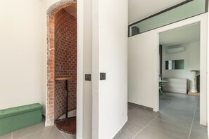 Ein Korridor mit Kamin aus Ziegelsteinen, einer grünen Bank und einer weißen Wand mit einer Tür zu einem anderen Raum.
