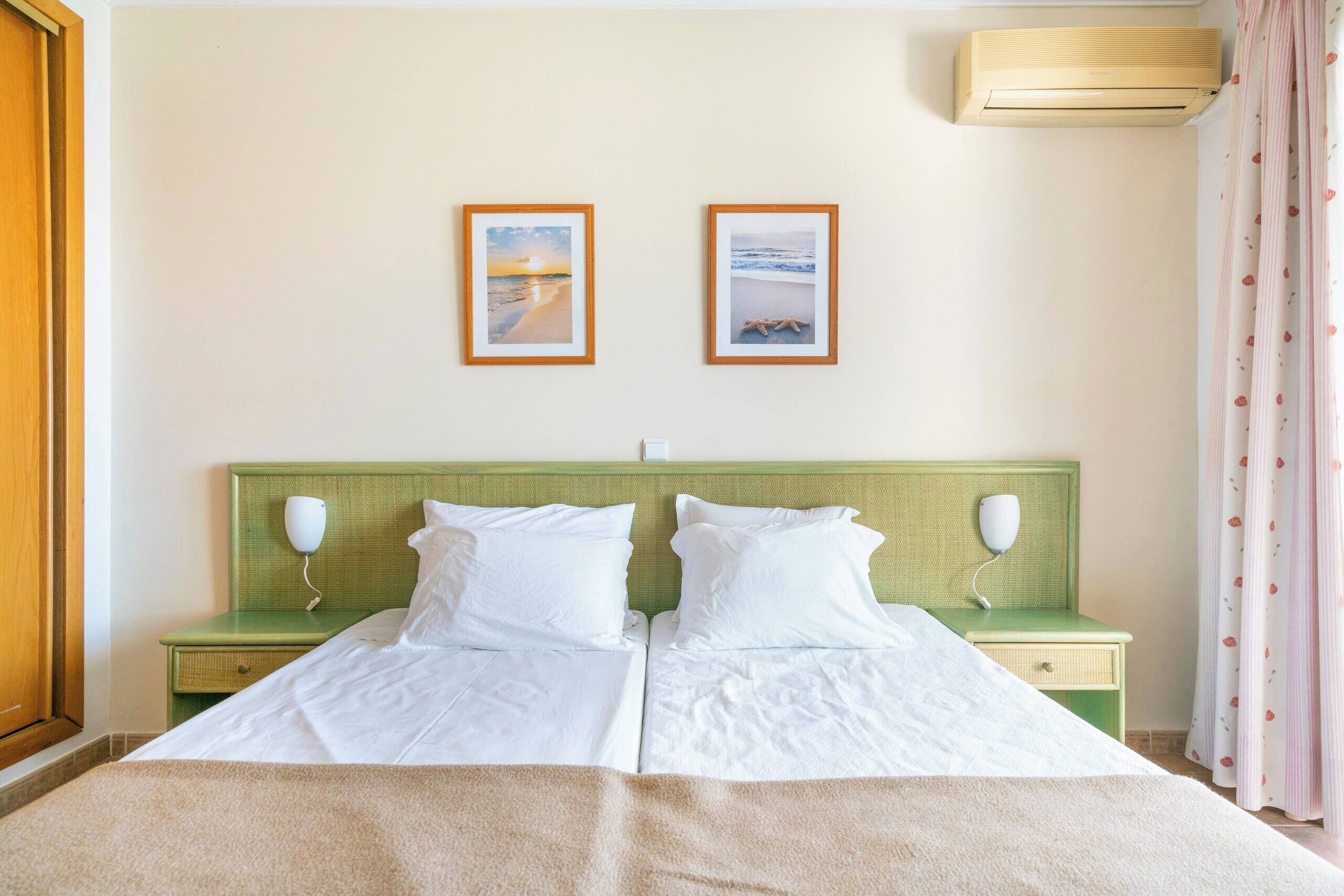 A double bed with white linens, two bedside tables with lamps, a green headboard, and two framed pictures on the wall.