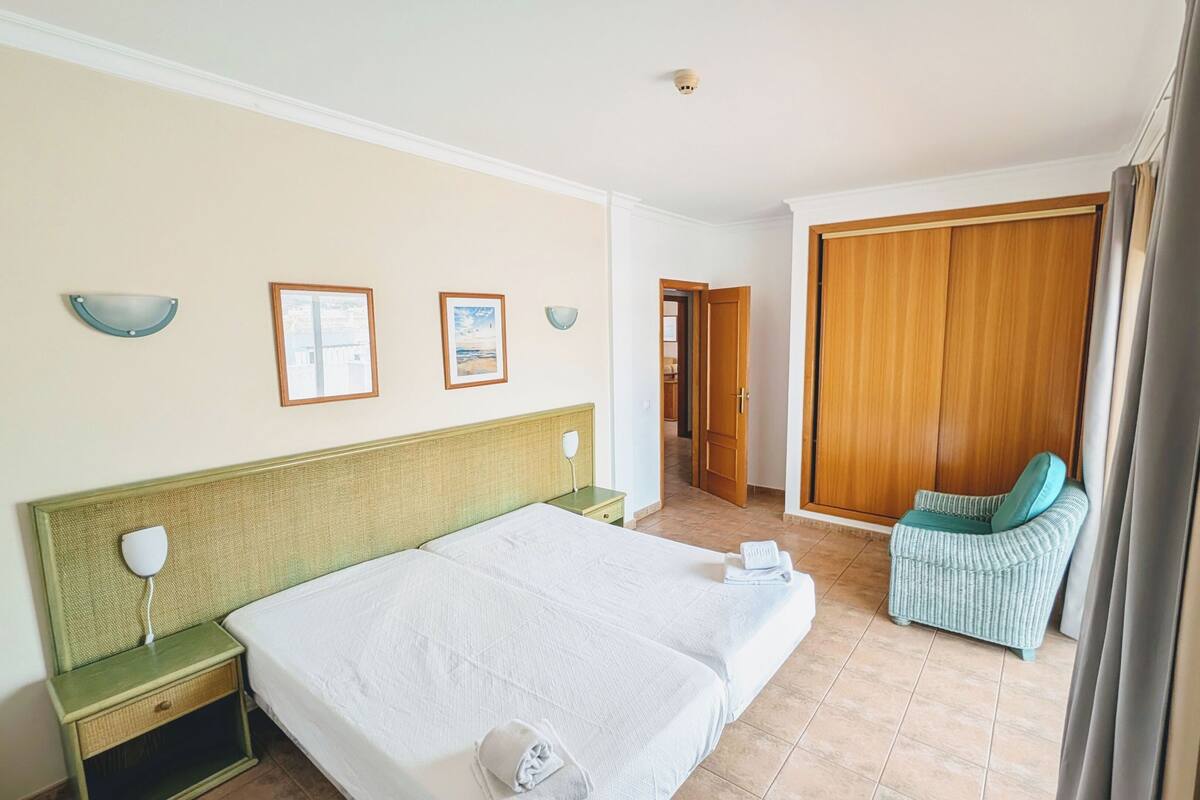 Habitación de hotel con una cama grande, una silla, un armario y un baño visible a través de una puerta abierta.