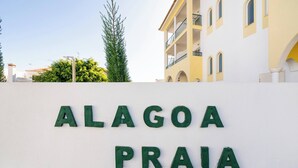 Un cartel con 'ALAGOA PRAIA' escrito en letras verdes sobre una pared blanca.