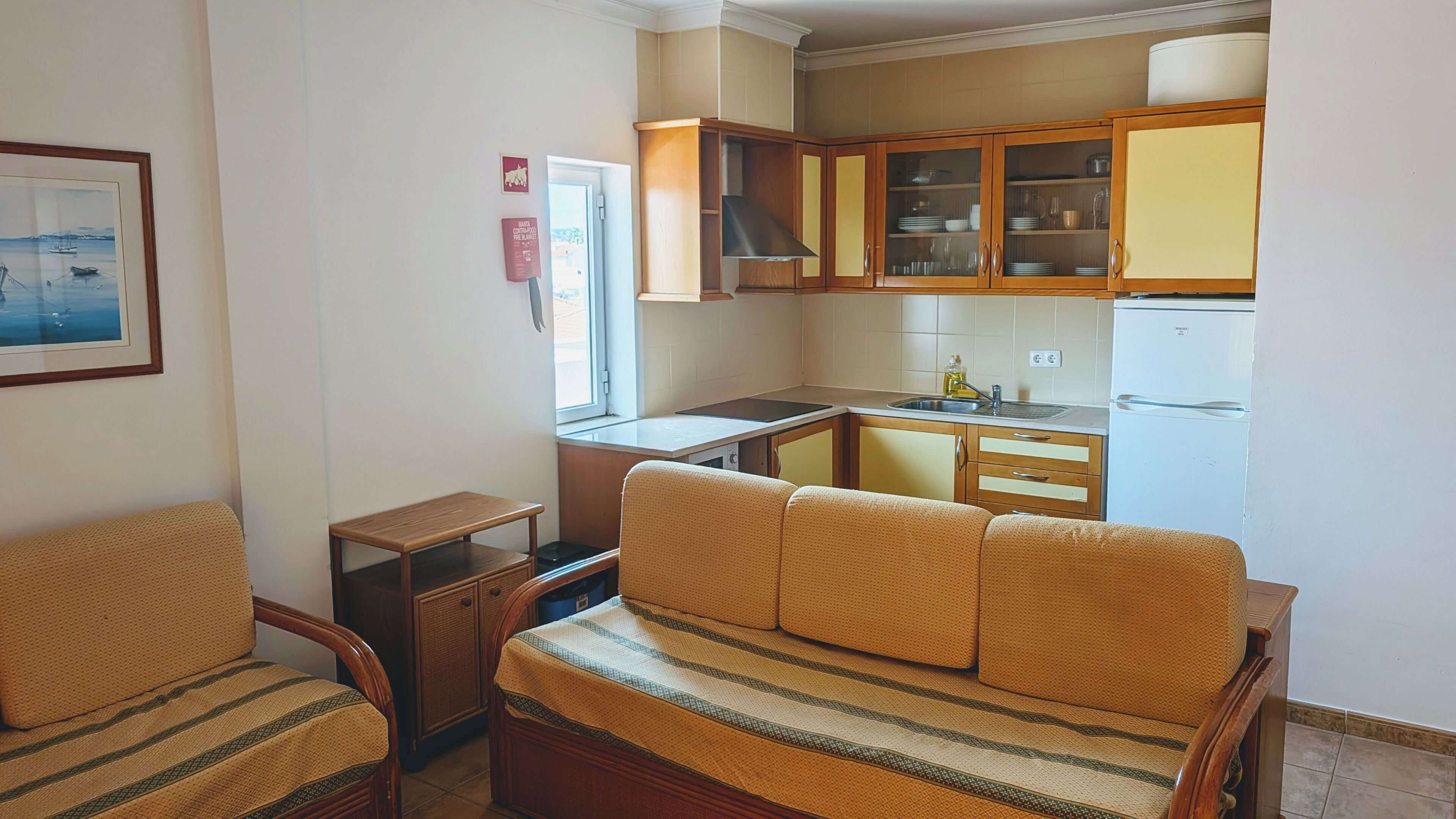 A compact living space with a kitchenette, a sofa, a small table, and a framed picture on the wall.