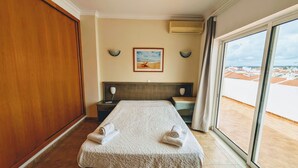 Una habitación de hotel con cama, mesita de noche, cabecero, ventana con vistas y un equipo de aire acondicionado.