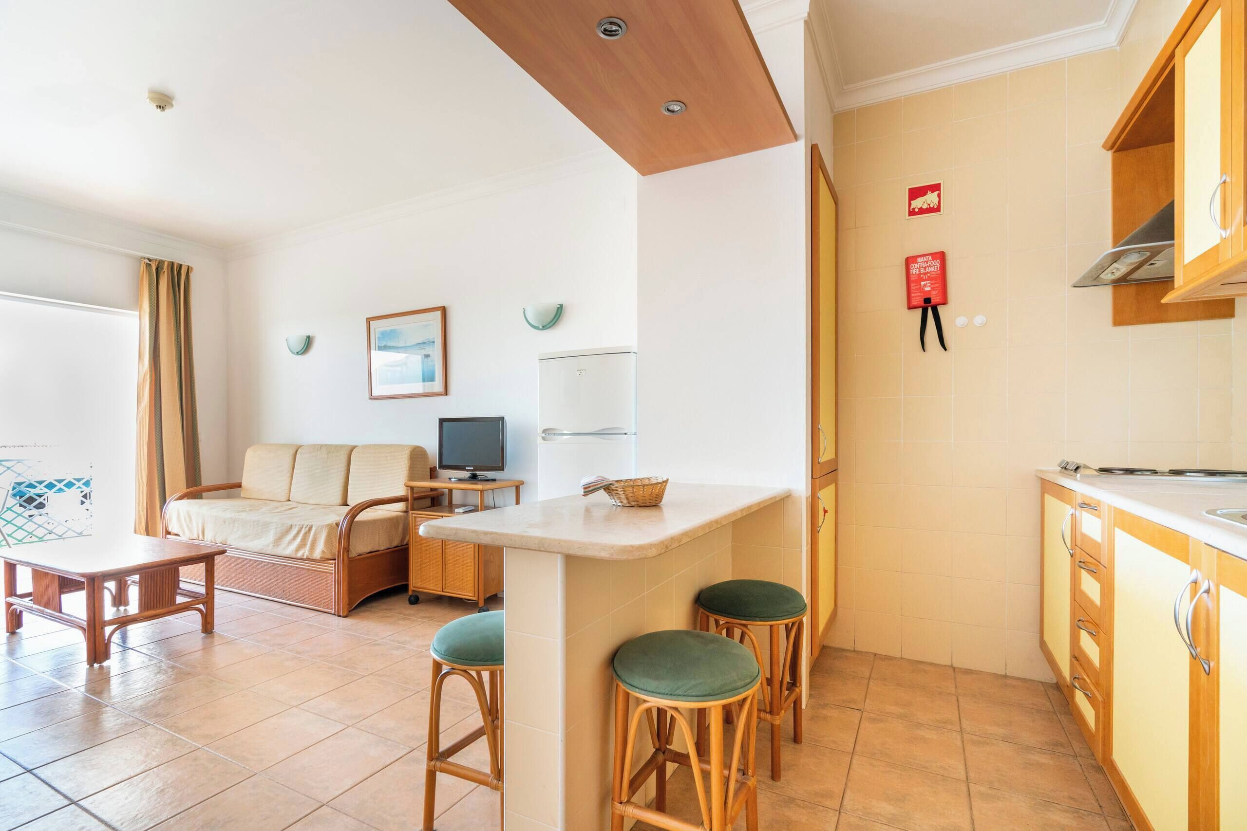 Un espacio habitable compacto con kitchenette, un sofá, una pequeña mesa de comedor y un televisor.