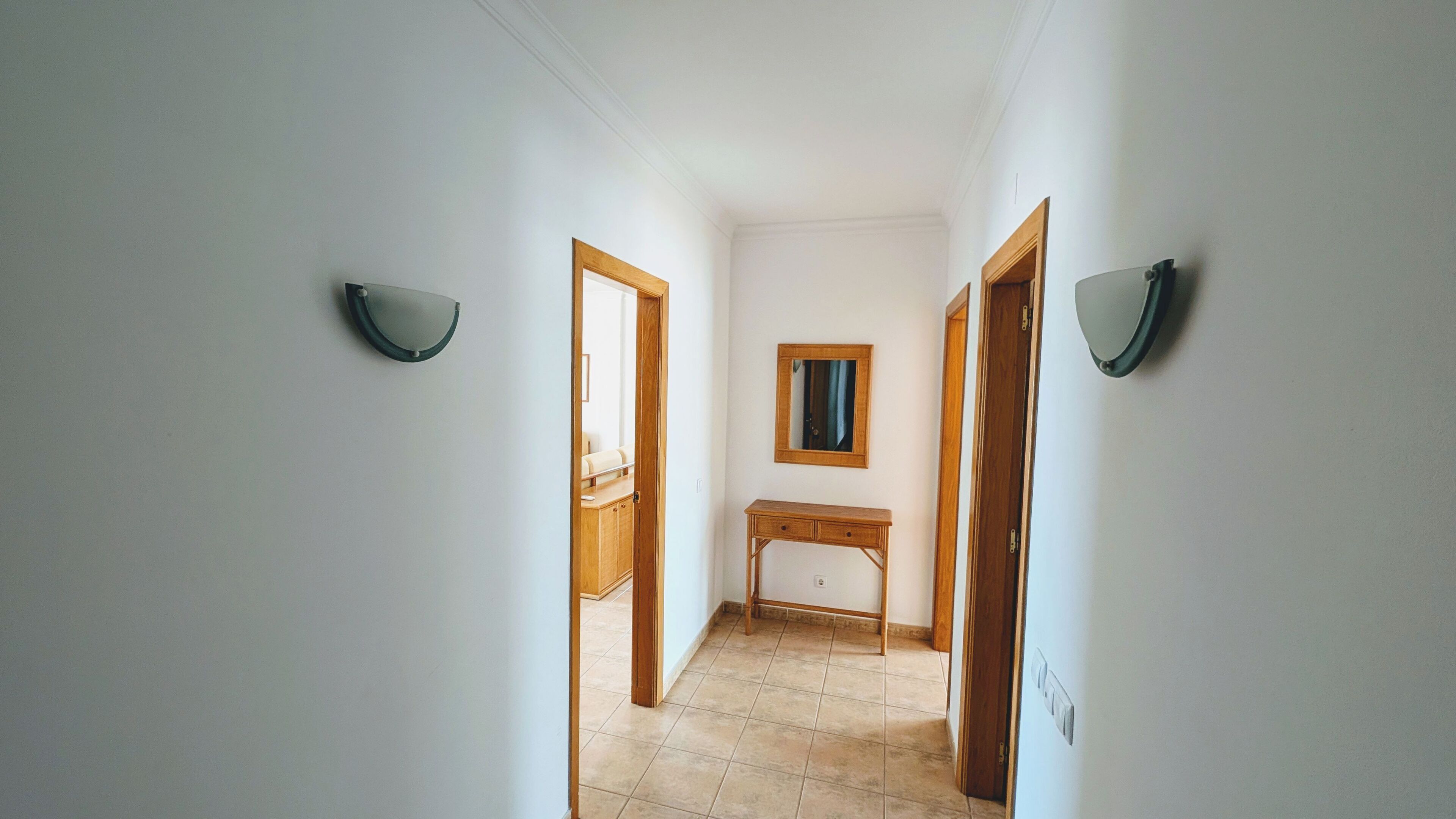 Un corridoio con pareti bianche, una scrivania in legno e due porte.