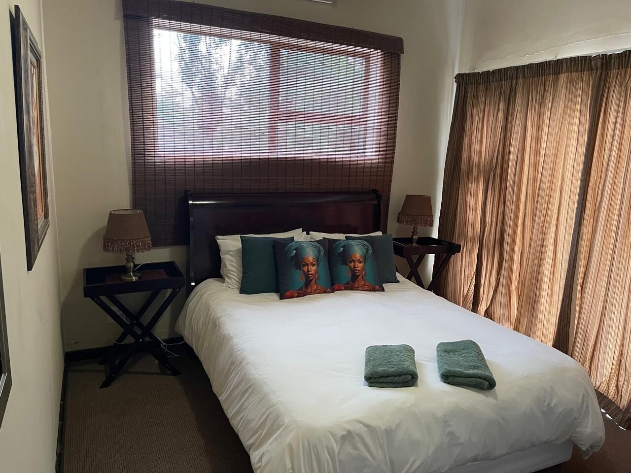 A hotel room with a bed, two bedside tables, a window with blinds, and a curtain.