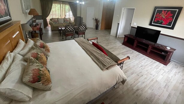 A hotel room with a large bed, a TV, a wooden entertainment unit, a dining area with a table and chairs, and a view of the outdoors.