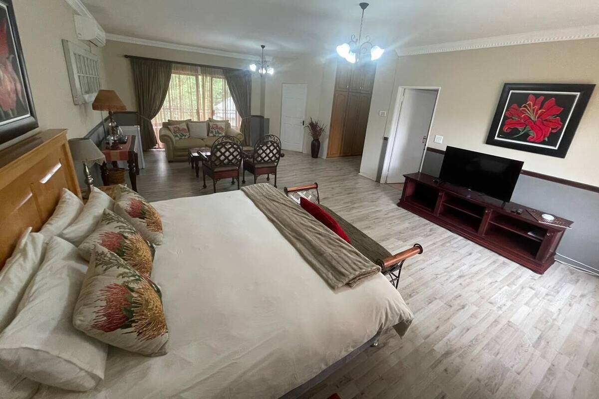 Habitación de hotel con una cama grande, televisión, mueble de entretenimiento de madera, zona de comedor con mesa y sillas, y vistas al exterior.