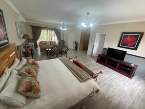 A hotel room with a large bed, a TV, a wooden entertainment unit, a dining area with a table and chairs, and a view of the outdoors. - Die Groen Akker  (Bloemfontein)