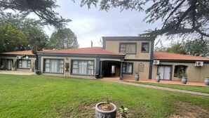 Un edificio de dos pisos con techo de tejas rojas, ventanas grandes y un patio empedrado.