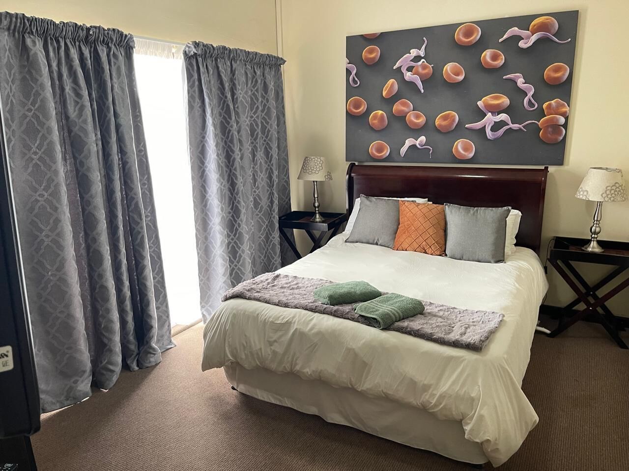 A hotel room with a bed, two nightstands, a lamp, a painting, and curtains.