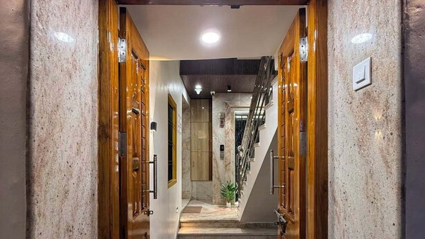 A hallway with wooden doors, a marble floor, and a staircase leading to an upper level. - Shree Villa Guest House (Varanasi)