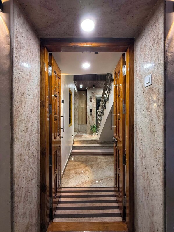 A hallway with wooden doors, a marble floor, and a staircase leading to an upper level. - Shree Villa Guest House (Varanasi)