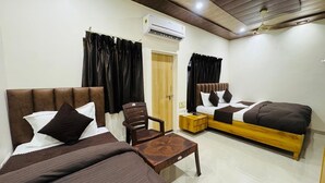A hotel room with a bed, a sofa, a chair, a small table, an air conditioning unit, and a door. - Shree Villa Guest House (Varanasi)