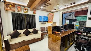 A modern living room with a sofa, a wooden desk, a television, and a computer. - Shree Villa Guest House (Varanasi)