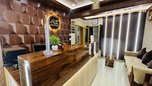 A reception desk with a wooden finish, a clock, and a plant. - Shree Villa Guest House (Varanasi)