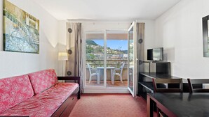 Ein Hotelzimmer mit einem roten Sofa, einem Fernseher, einem Balkon mit Blick auf eine Hügelterrasse und einem Bild an der Wand.