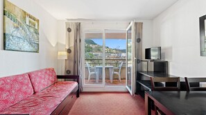 Ein Hotelzimmer mit einem roten Sofa, einem Fernseher, einem Balkon mit Blick auf eine Hügelterrasse und einem Bild an der Wand.