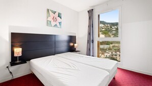 Ein Hotelzimmer mit einem großen Bett, zwei Nachttischlampen, einem Fenster mit Blick auf Gebäude und einem floralen Kunstwerk an der Wand.