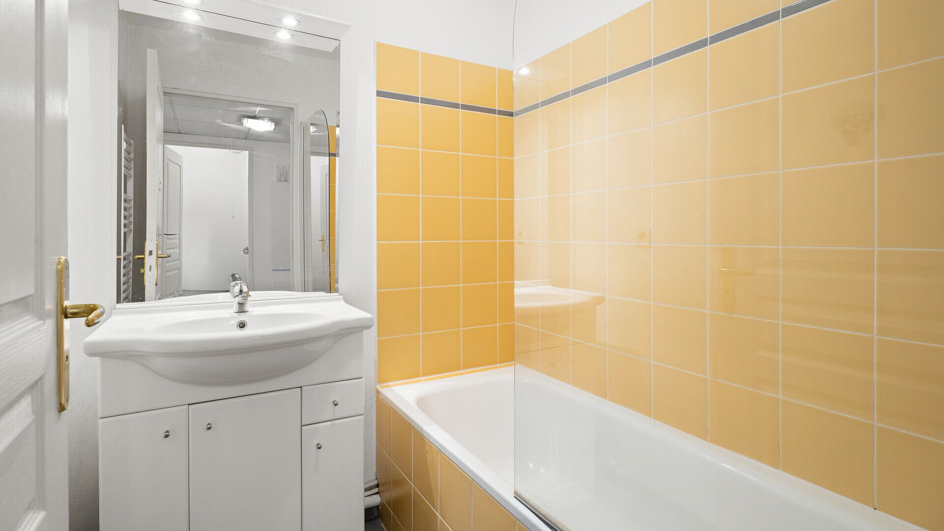 Un baño con un lavamanos blanco, un espejo, una bañera y paredes con azulejos amarillos.