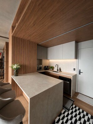 A modern kitchen with a central island, wooden paneling, and a black and white patterned rug. - Millenium Luxury | Cozy Studio in Vila Olímpia (São Paulo)