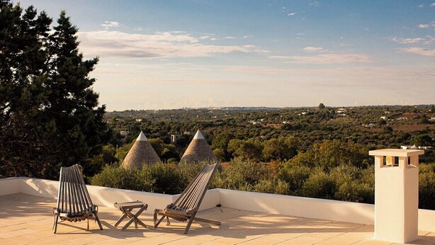 Eine Terrasse mit zwei gestreiften Liegestühlen, einem kleinen Tisch und Blick auf eine ländliche Landschaft mit Häusern mit Kegeldächern.