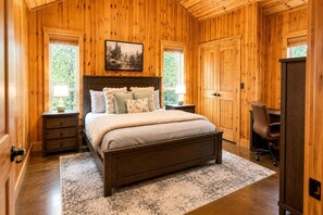A wooden-paneled bedroom with a bed, bedside tables, a desk, and a chair. - Luxury Group Cabin with Hot Tub & Media Room in Broken Bow, OK (Broken Bow)
