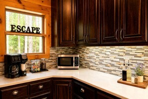 A kitchen with dark wood cabinets, a coffee maker, a microwave, and a window with 'ESCAPE' written on it. - Luxury Group Cabin with Hot Tub & Media Room in Broken Bow, OK (Broken Bow)