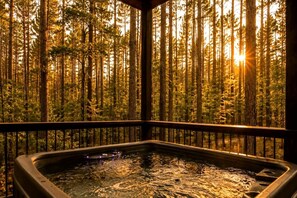 A hot tub with a forest view, surrounded by a wooden deck and railing. - Luxury Group Cabin with Hot Tub & Media Room in Broken Bow, OK (Broken Bow)