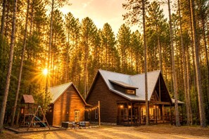 A cabin with a sloped roof, a porch with seating, and a swing set in a forest. - Luxury Group Cabin with Hot Tub & Media Room in Broken Bow, OK (Broken Bow)
