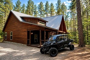 Eine Blockhütte mit Metalldach, einer Veranda und einem schwarzen Geländewagen davor geparkt.