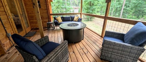 A wooden deck with wicker furniture and a round table, surrounded by a wooden cabin structure.