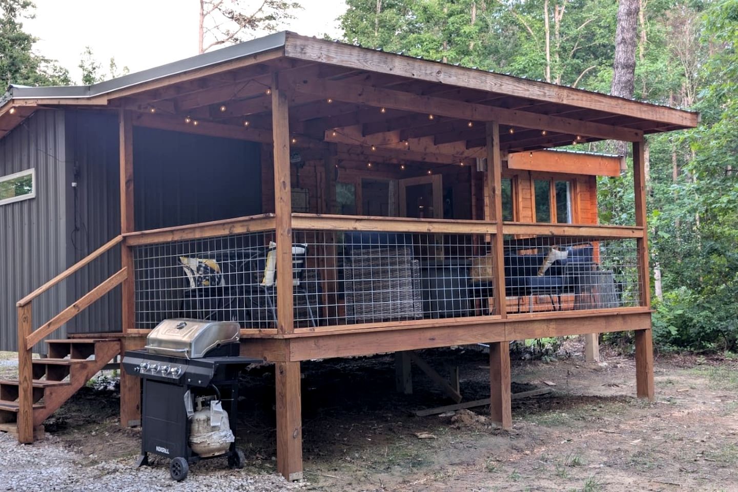 A wooden cabin with a covered porch, a grill, and a trash bin.