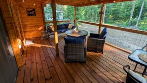 Eine Holzterrasse mit Korbmöbeln, einer Feuerstelle und Blick auf den Wald.