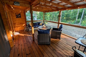 Een houten terras met rieten meubels, een vuurkorf en uitzicht op het bos.