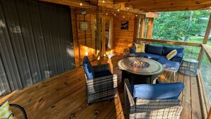 Eine Holzhütte mit einer Terrasse, Korbmöbeln, einer Feuerstelle und einer Veranda.