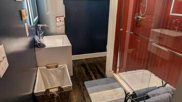 Un bagno compatto con doccia, lavandino, una piccola finestra e pavimento in legno.