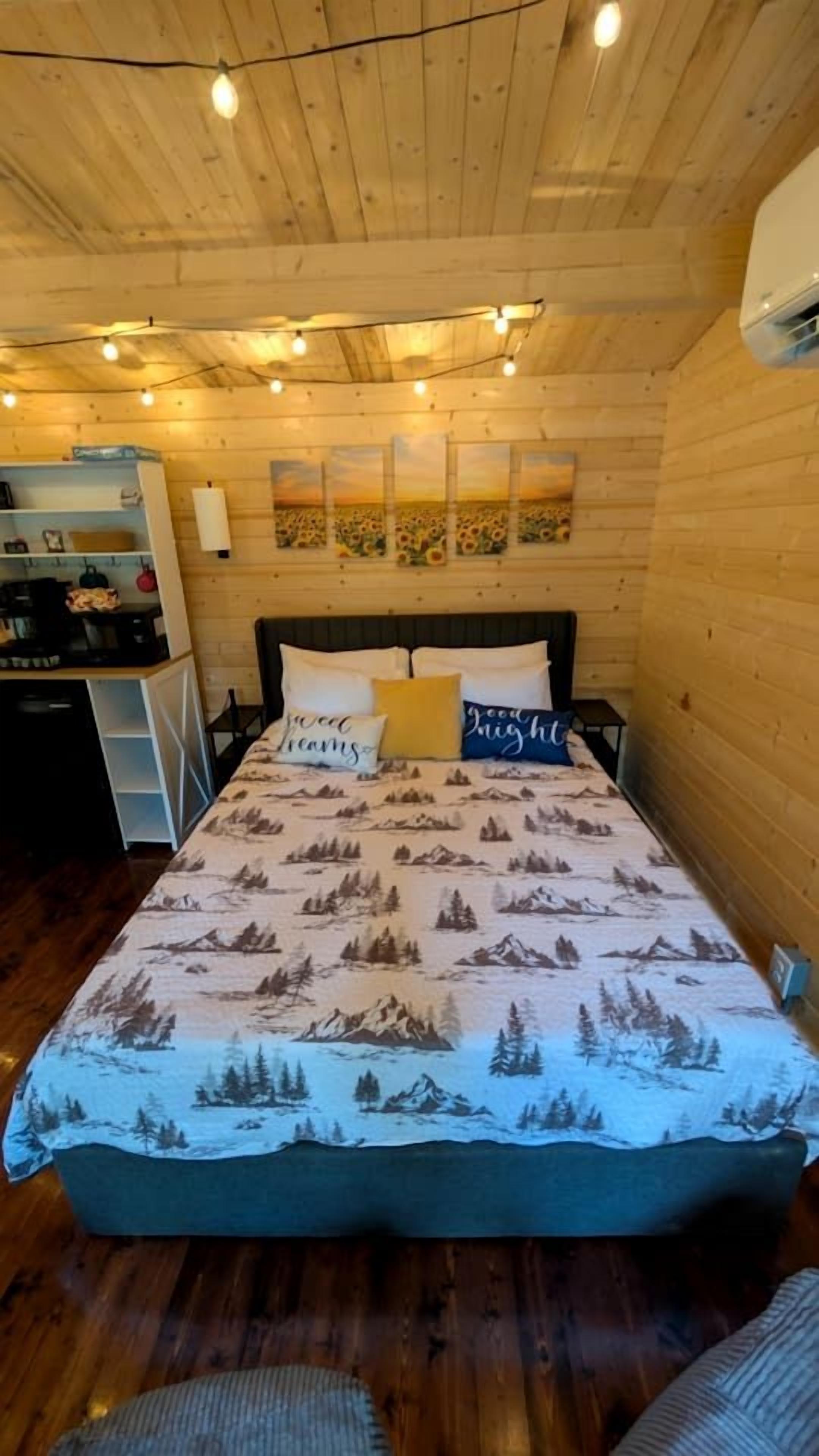 A wooden cabin room with a bed, a desk, and a wall-mounted air conditioner.
