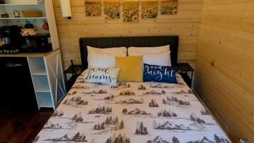 A wooden cabin room with a bed, a desk, and a wall-mounted air conditioner.