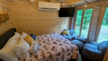 Een slaapkamer in een houten chalet met een bed, een stoel, een televisie en een airconditioner.