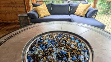 Una mesa redonda de vidrio con un mosaico de piezas de vidrio, un sofá azul con cojines amarillos y un interior de madera.