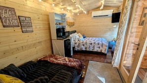 Ein Ferienhäuschen mit einer Couch, einem Bett, einer kleinen Küchenzeile und Holzwänden.