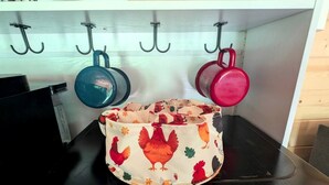 A kitchen with a stove, a hanging pot rack, and a colorful cloth bag on the counter. - Luxury Woodland Cabin Near The Caverns & Savage Gulf, Tennessee (Coalmont)