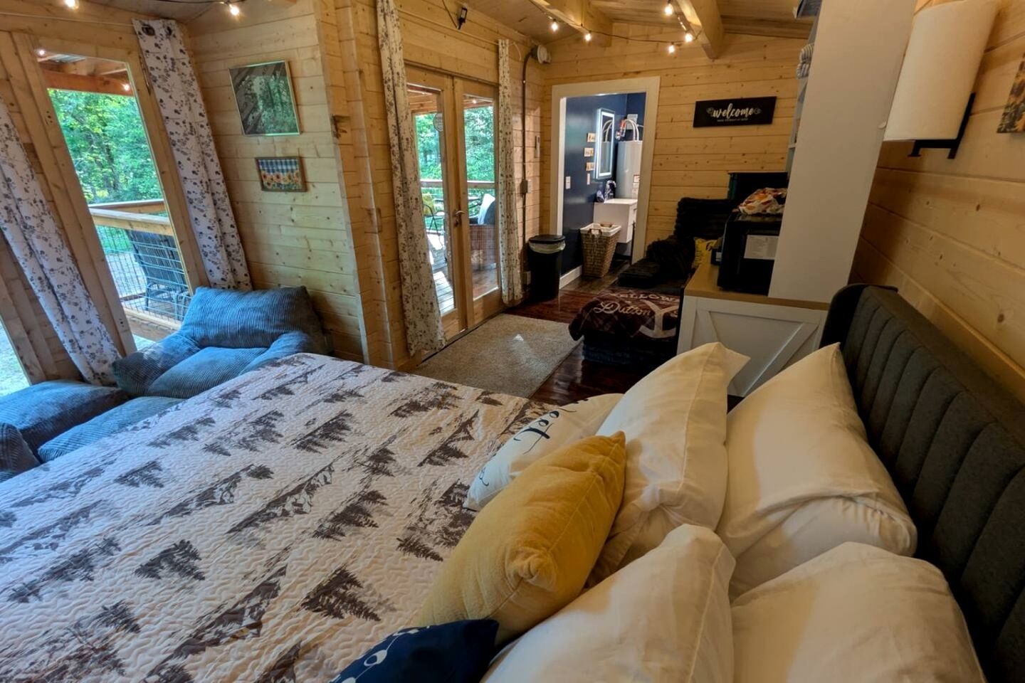 A wooden cabin room with a bed, a small kitchenette, and a view of the outdoors.