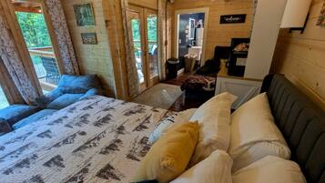 A wooden cabin room with a bed, a small kitchenette, and a view of the outdoors.
