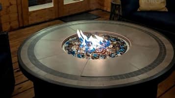 A circular stone fire pit with a fire, surrounded by wooden walls and a wooden door with glass panels.