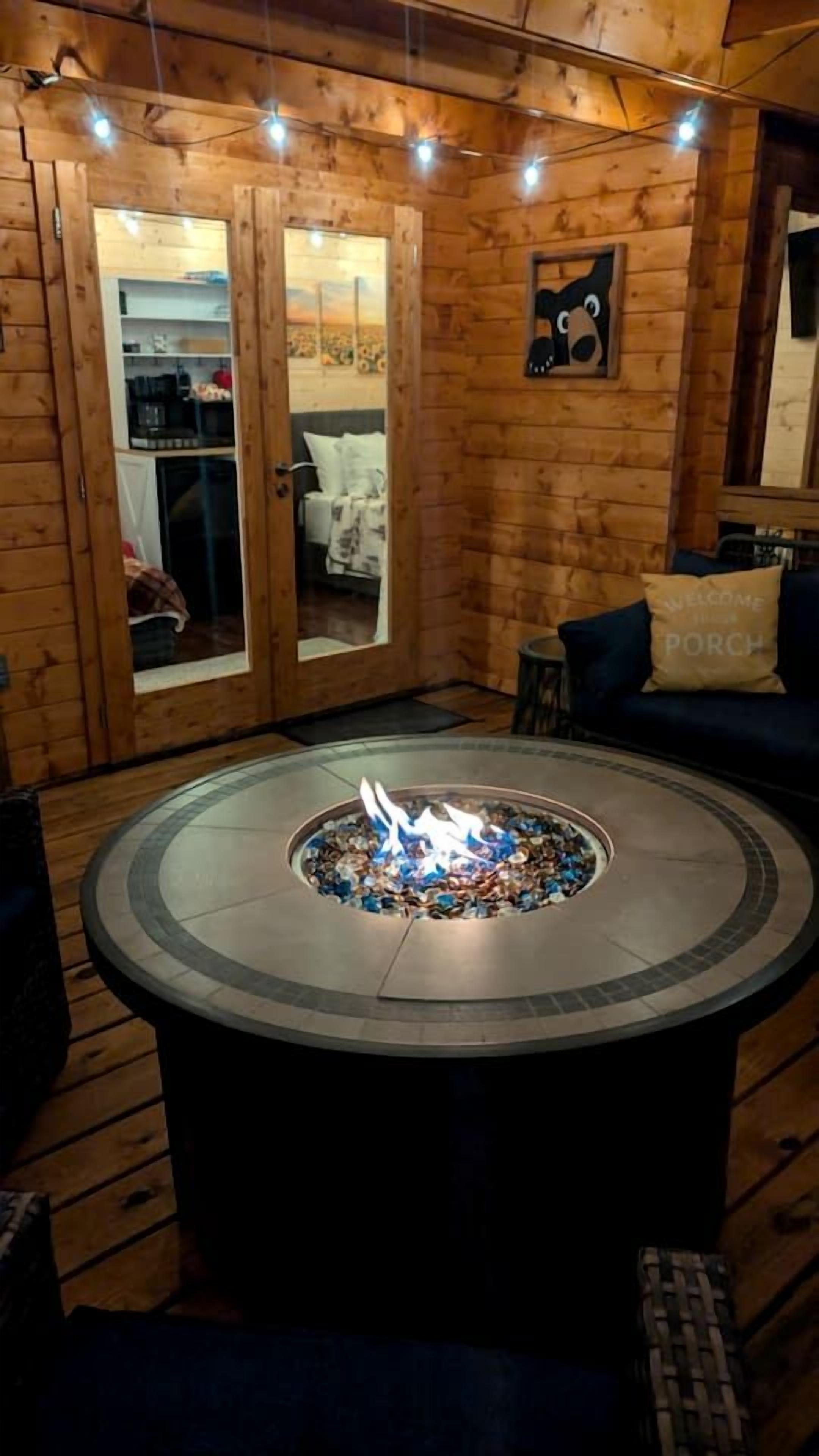 Un foyer circulaire en pierre, avec un feu au centre, entouré de murs en bois et doté d’une porte en bois avec des panneaux de verre.
