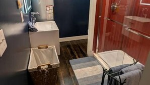 Ein kleines Badezimmer mit Dusche, Waschbecken, einem kleinen Fenster und Holzboden.