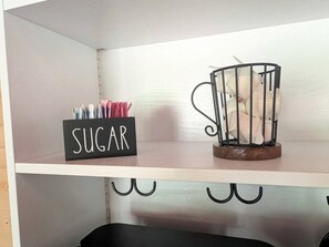 En hylde med et skilt der står 'SUGAR', en metalkopholder og en sort beholder.