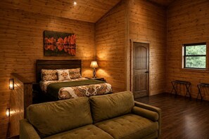 Ein Schlafzimmer in einer Blockhütte mit Bett, einer Couch, einem Gemälde, einem Fenster und einer Tür.
