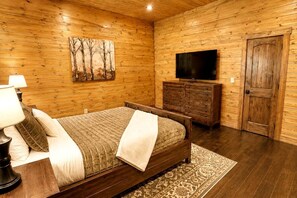 Ein Schlafzimmer mit Holzwänden, einem Bett, einem Schminktisch, einem Fernseher und einer Tür.